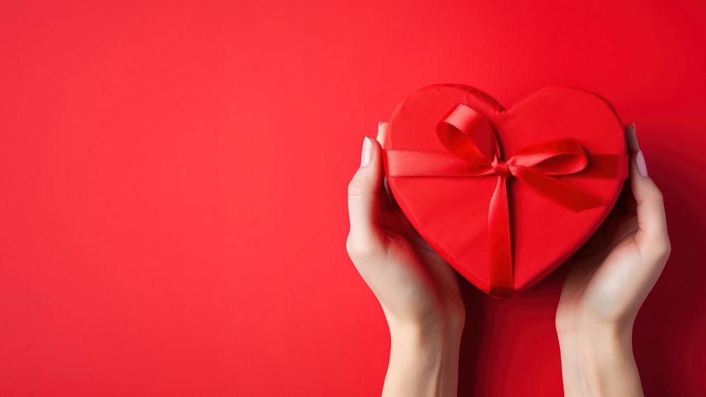 A photo of hands of woman holding a nice shape valentines present on red background.  