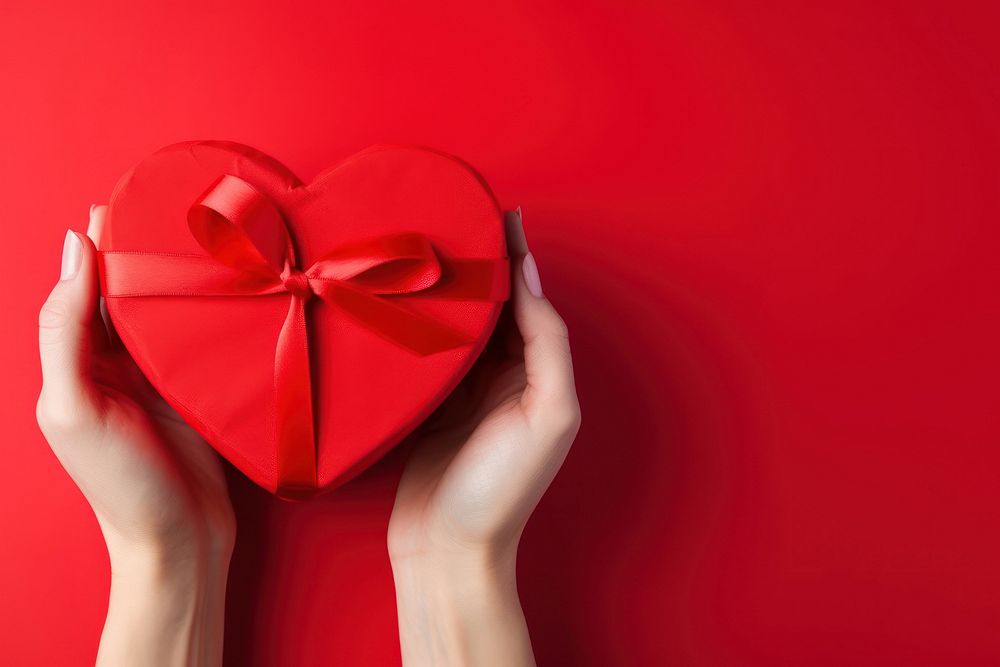 A photo of hands of woman holding a nice shape valentines present on red background.  