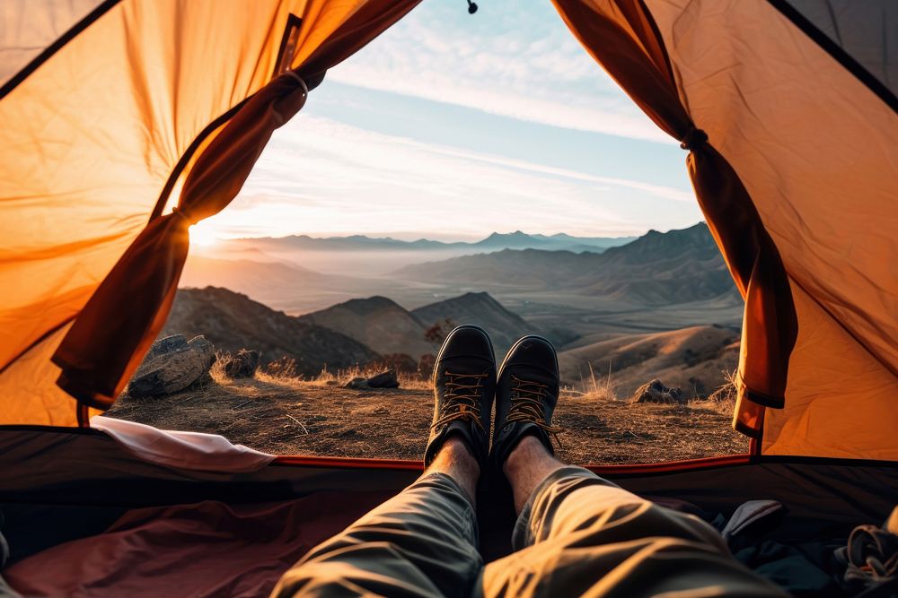 Photo of a foot of a man wearing boots stretching out of a tent, mountain view.  