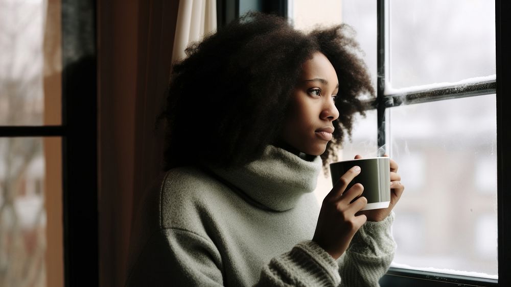 Photo of Thoughtful black woman with coffee cup looking through window in winter season.  