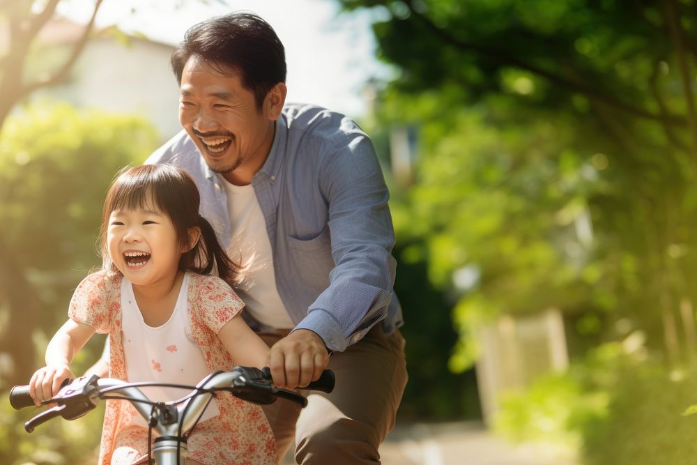 photo of an Asian father helps young daughter ride a bicycle.  