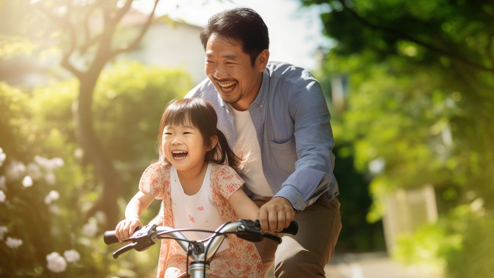 photo of an Asian father helps young daughter ride a bicycle.  