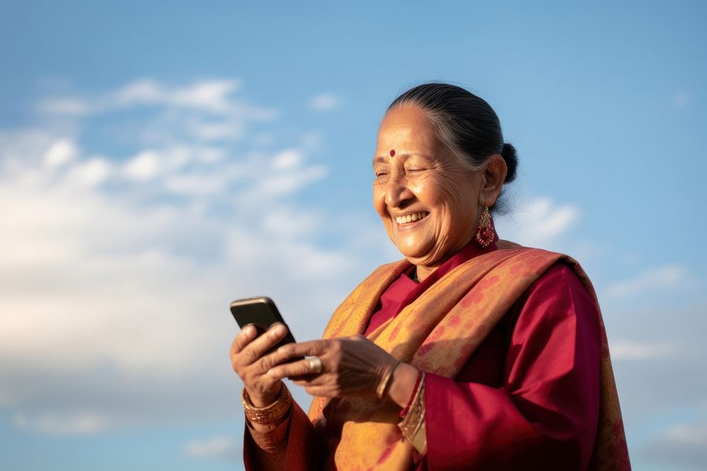 Senior indian business woman using smartphone facetiming adult photo sky. AI generated Image by rawpixel.