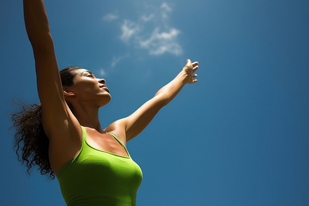 photo of mid-ages woman stretch the arms with bluesky and sun the green natual with blurred visio.  