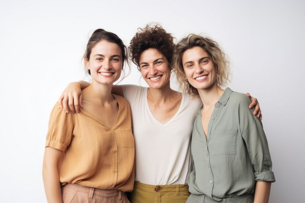 Three smiling women standing together, embracing. Casual attire, relaxed atmosphere. Neutral background, showcasing…