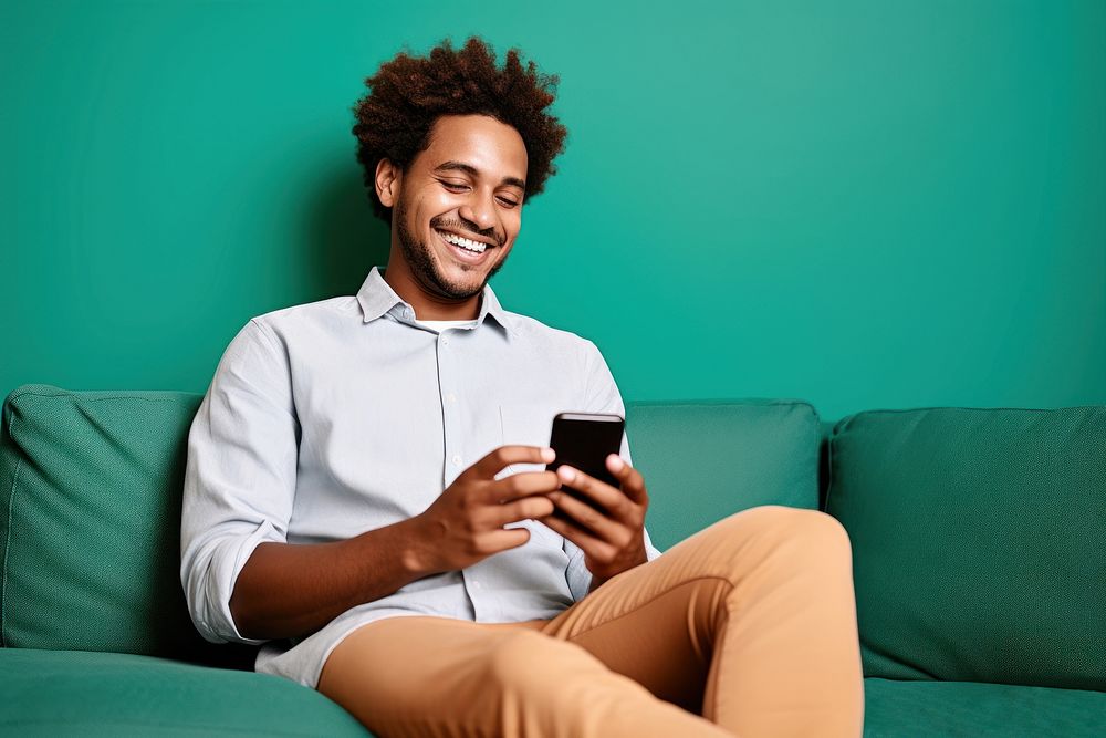 Happy young man using his cellphone while relaxing on the couch sitting portability technology. 