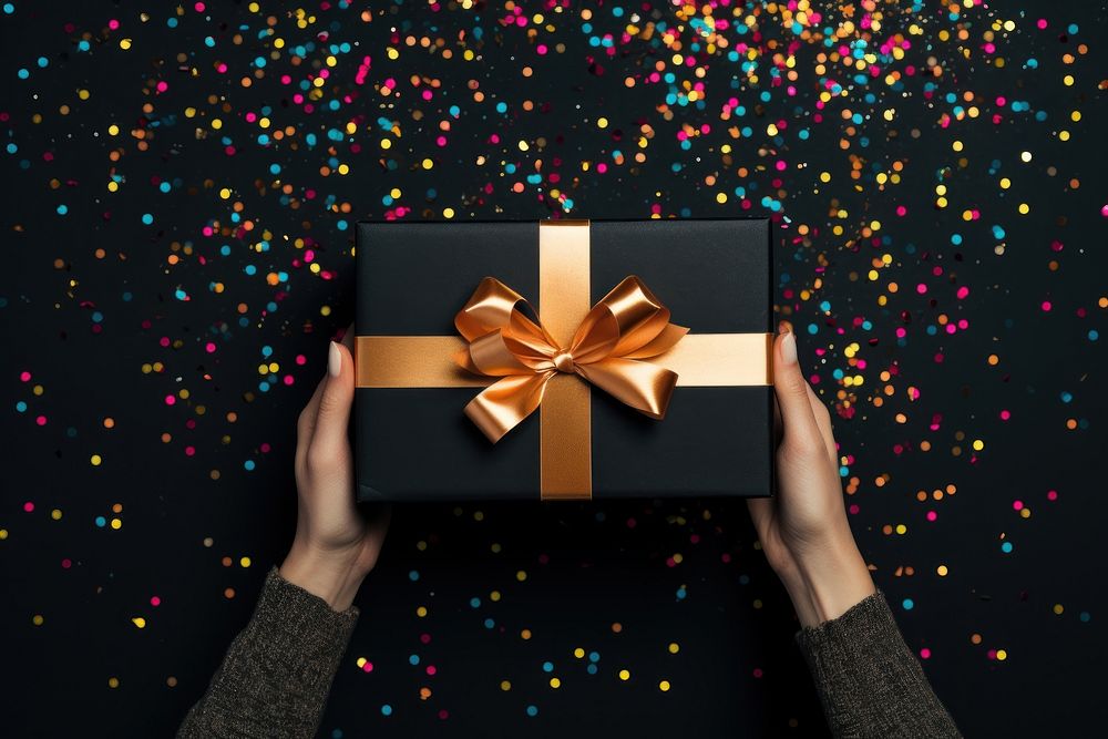 Holding gold present box confetti hand black background. AI generated Image by rawpixel.