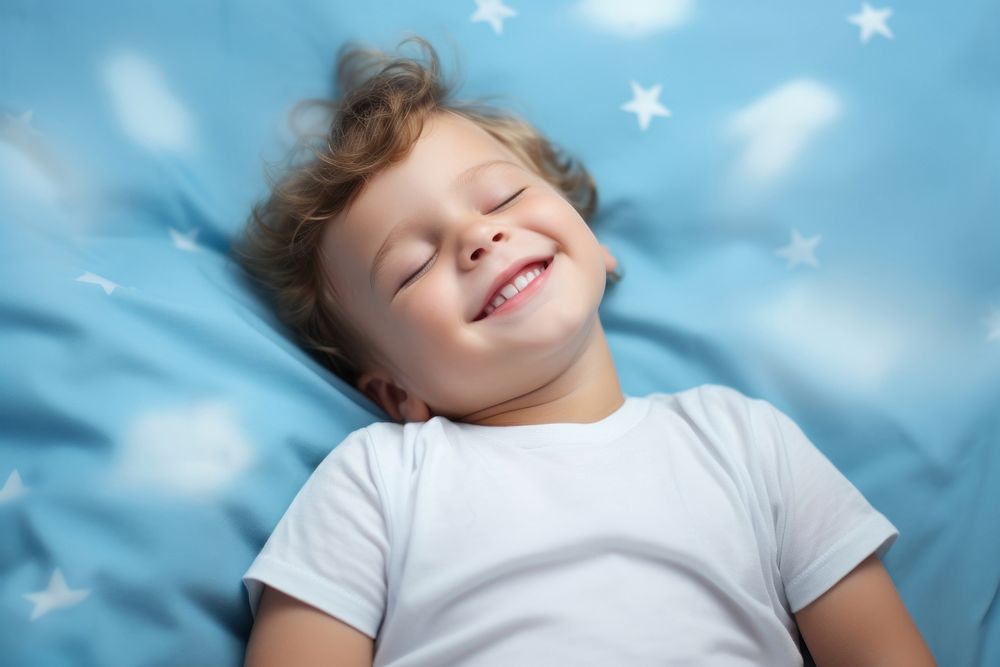 Smiling baby boy lying on a bed sleeping on blue sheets smiling smile comfortable. AI generated Image by rawpixel.