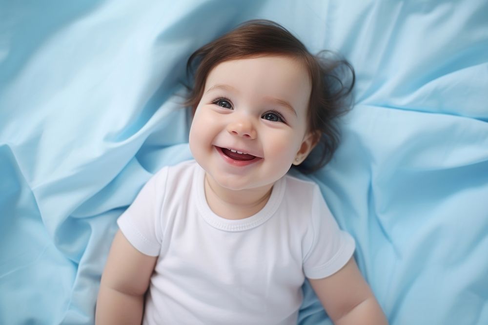 Smiling baby girl lying on a bed sleeping on blue sheets smiling smile beginnings. AI generated Image by rawpixel.