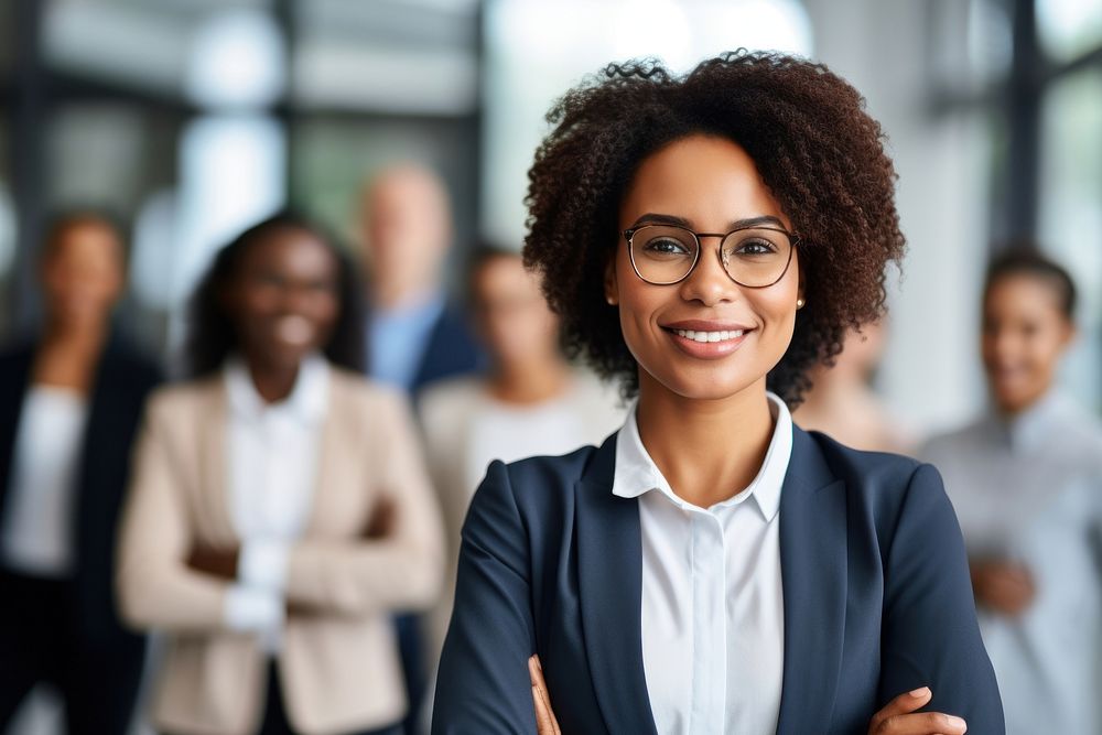 Smiling confident african business female leader looking at camera and standing in an office at team meeting smiling glasses…