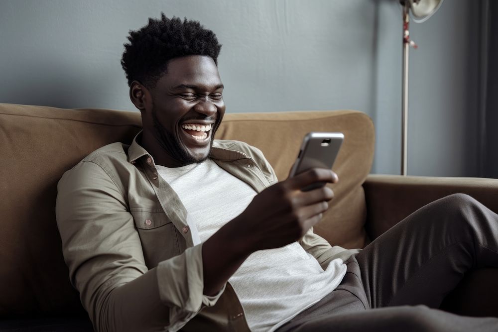 Happy relaxed african man using cell phone laughing sitting holding. AI generated Image by rawpixel.