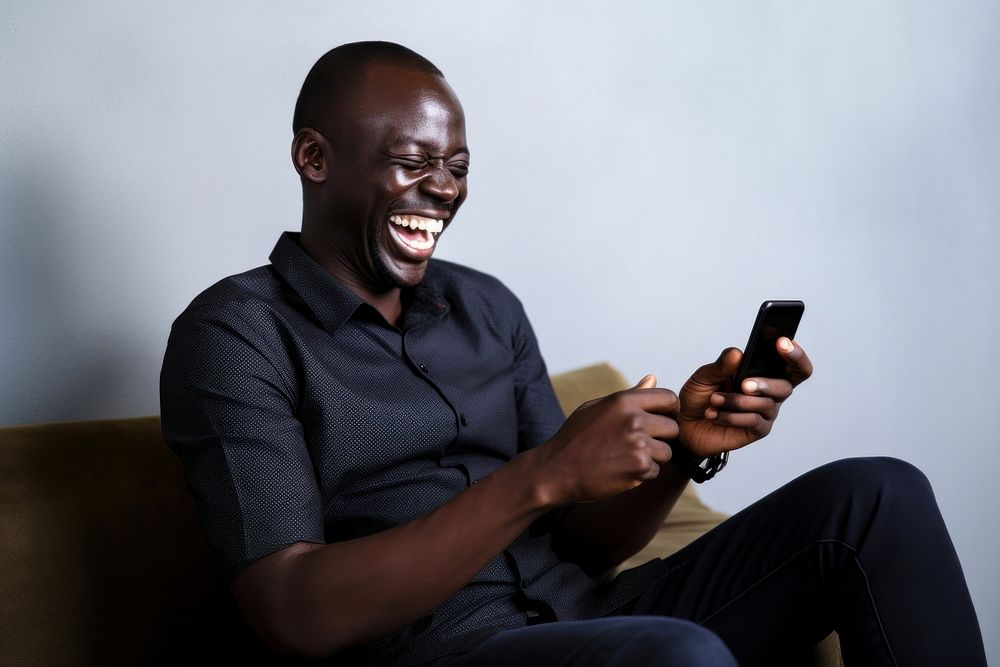 Happy relaxed african man using cell phone laughing sitting holding. AI generated Image by rawpixel.