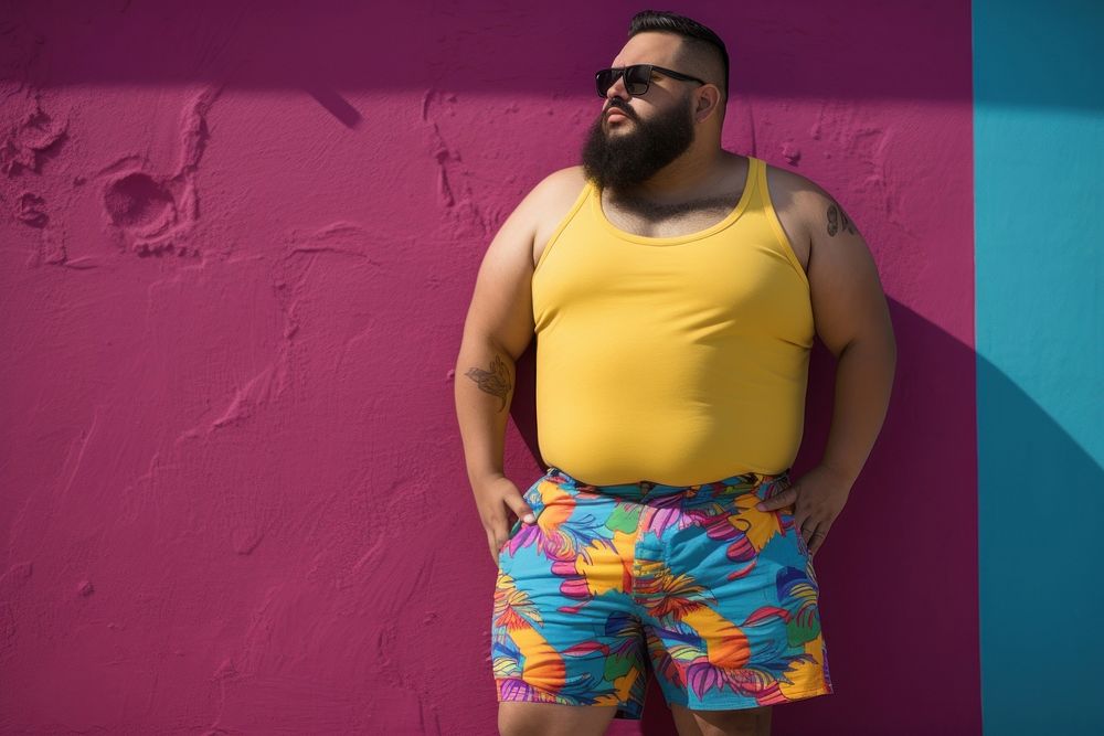 Plus size Latino man in a swimming pants standing in front of a colorful wall glasses fashion shorts. AI generated Image by…