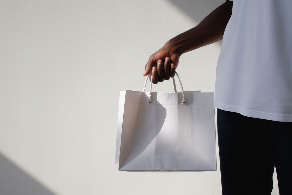 A man holding a white paper shopping bag handbag adult accessories. AI generated Image by rawpixel.