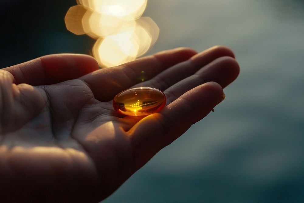 Hand holding fish oil pill illuminated reflection medication. AI generated Image by rawpixel.