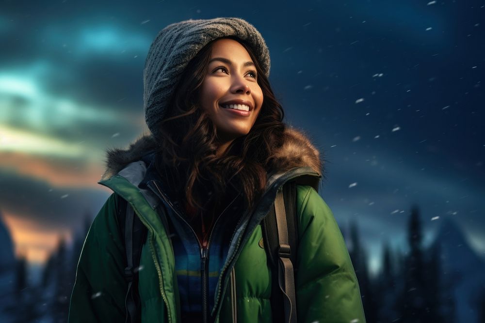 A Latina Colombian female backpacker sitting and joyfully looking at the northern lights in the sky in Alaska portrait…