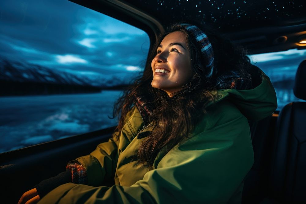 A Latina Colombian female backpacker sitting and joyfully looking at the northern lights in the sky in Alaska portrait…