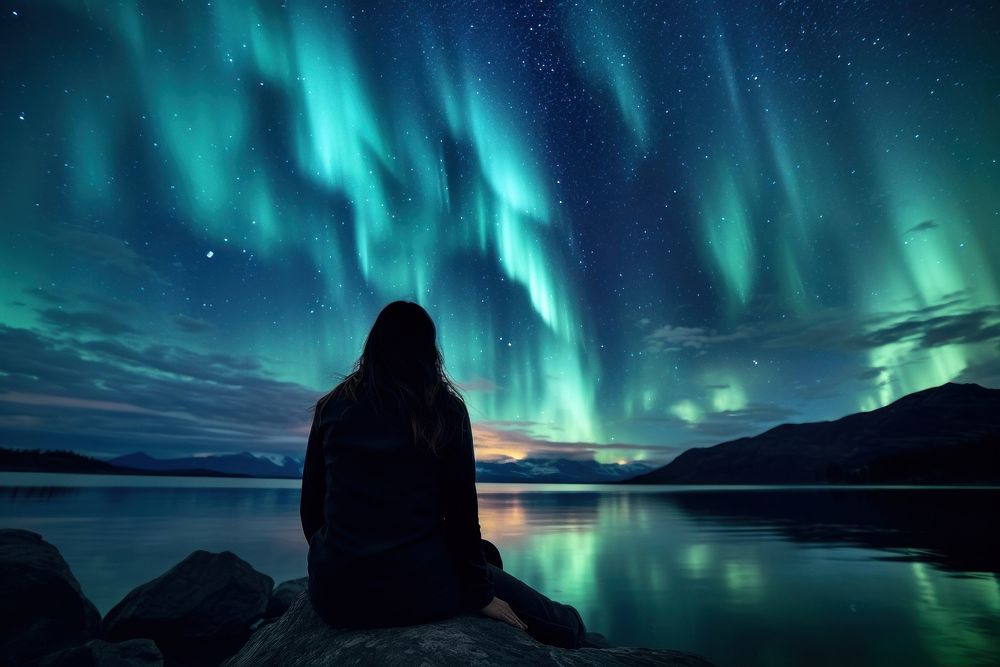 A Latina Mexican female backpacker sitting and joyfully looking at the northern lights in the sky in Alaska nature outdoors…