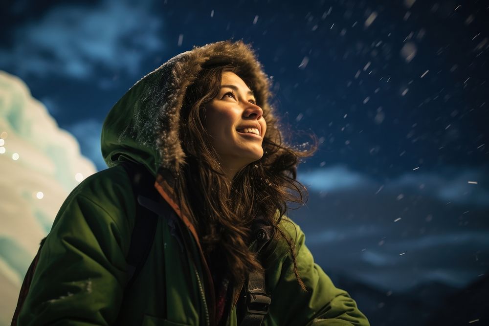 A Latina Mexican female backpacker sitting and joyfully looking at the northern lights in the sky in Alaska nature portrait…