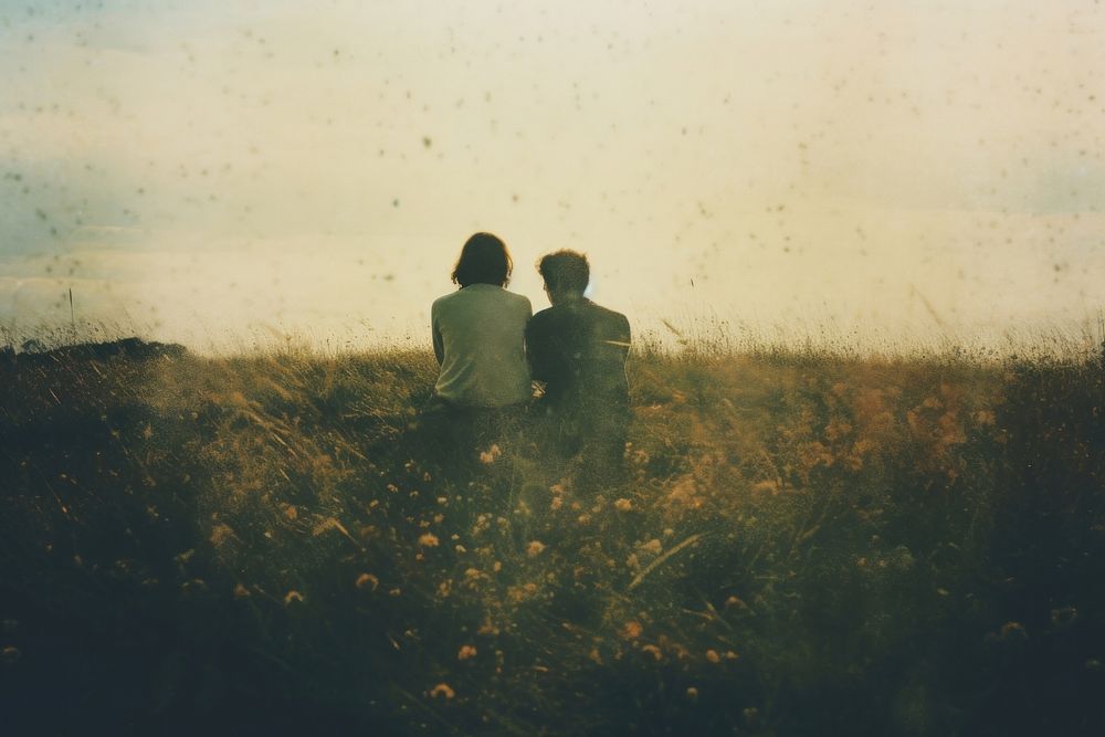 A far away couple sitting on top a grass covered field photography landscape outdoors. AI generated Image by rawpixel.