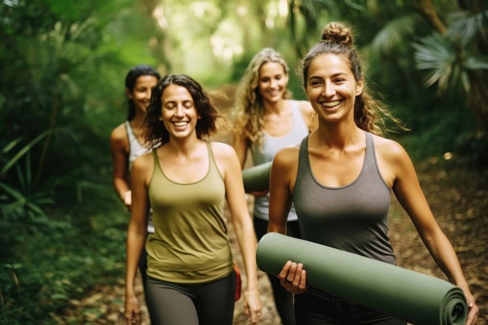 Smiling female friends carrying yoga matt walking through path in jungle laughing adult determination. AI generated Image by…