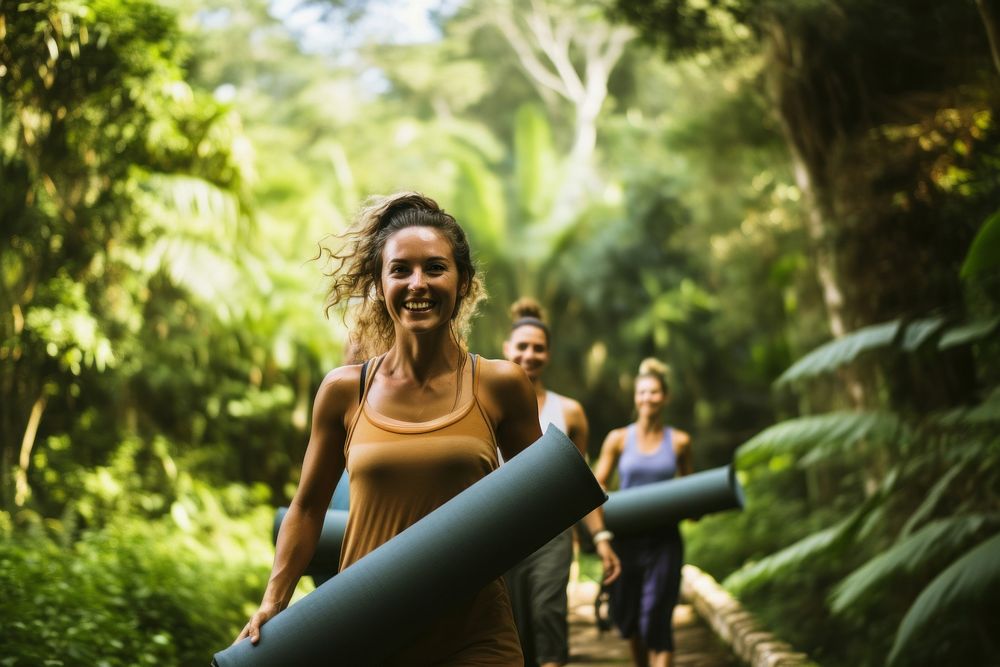 Smiling female friends carrying yoga matt walking through path in jungle outdoors nature plant. AI generated Image by…