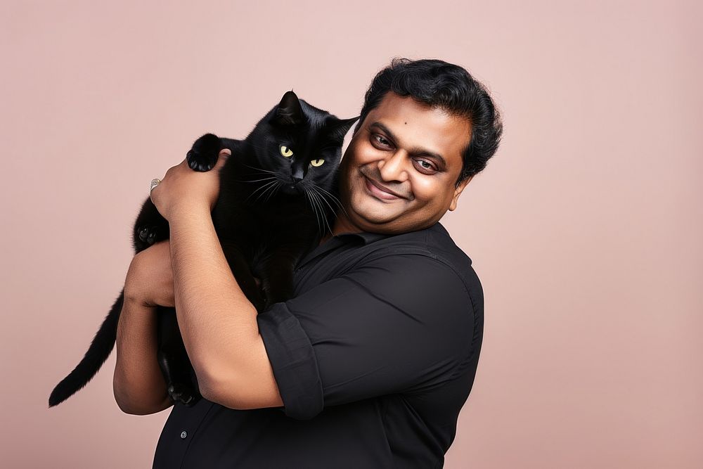 Indian middle age chubby man hugging black cat pet mammal animal. AI generated Image by rawpixel.