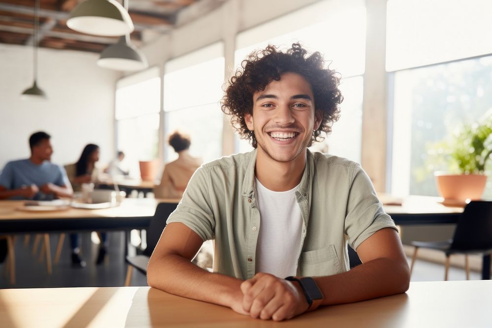 Latino student man sitting at table laughing in classroom person smile adult. AI generated Image by rawpixel.