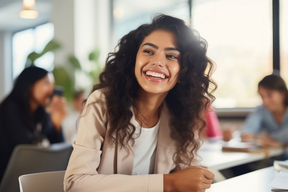 Latina student woman sitting at table laughing in classroom person smile adult. AI generated Image by rawpixel.