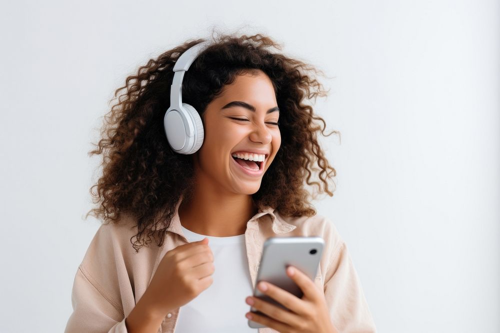 Young woman wearing headphones and playing phone laughing headset smile. AI generated Image by rawpixel.