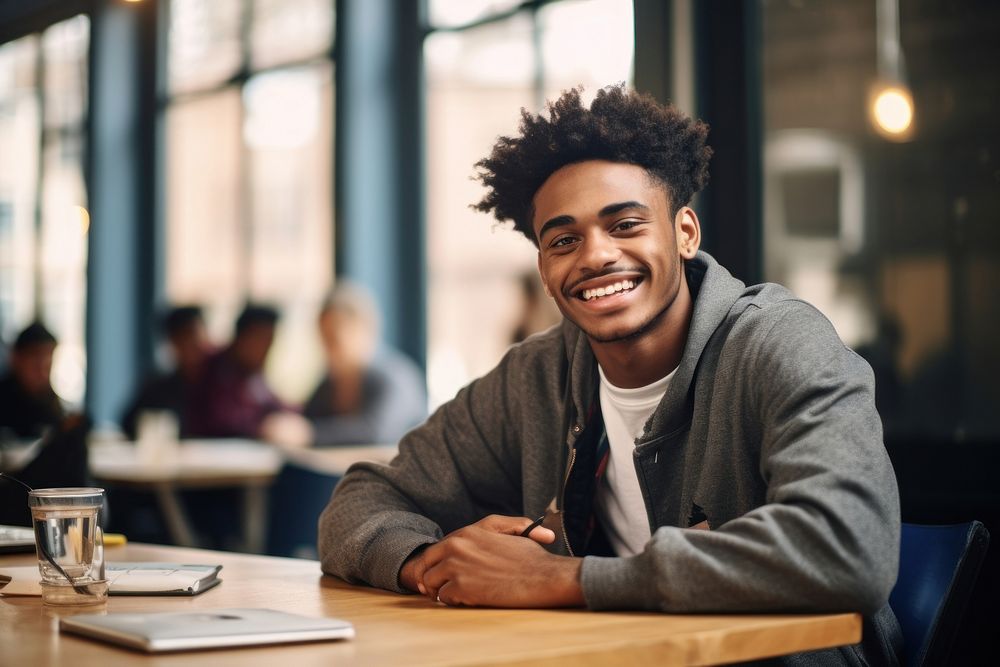 African American student man sitting at table laughing in classroom person smile architecture. AI generated Image by…