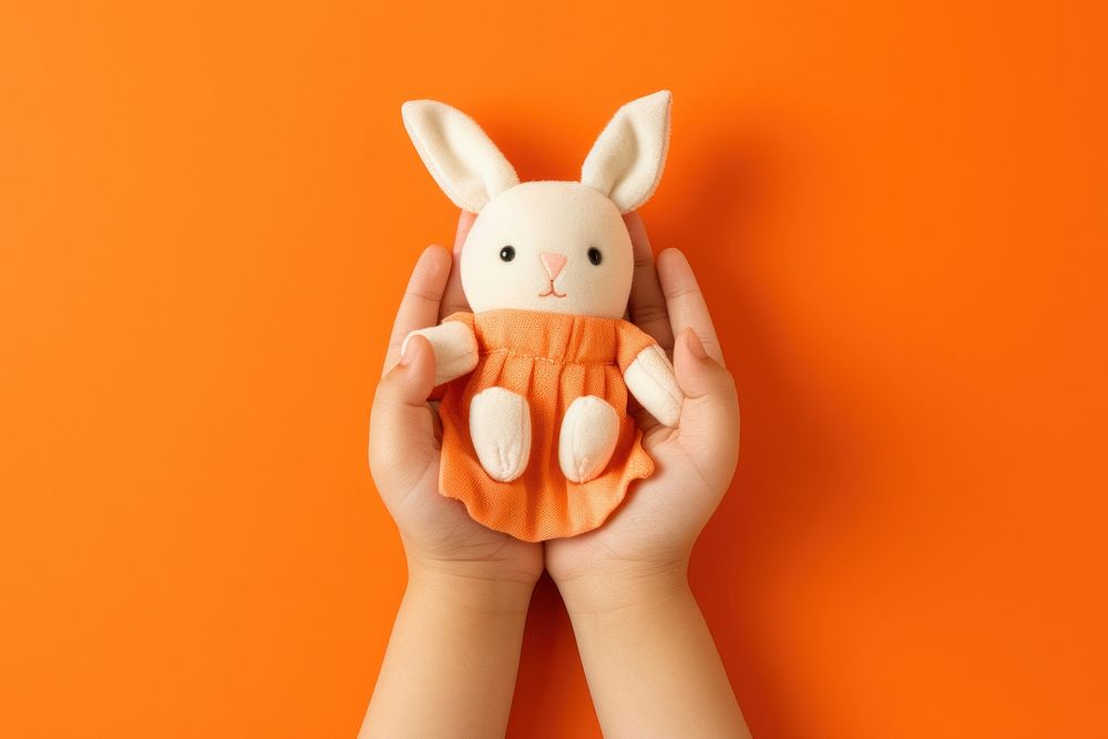 Baby hands holding fabric rabbit doll plush toy orange background. AI generated Image by rawpixel.