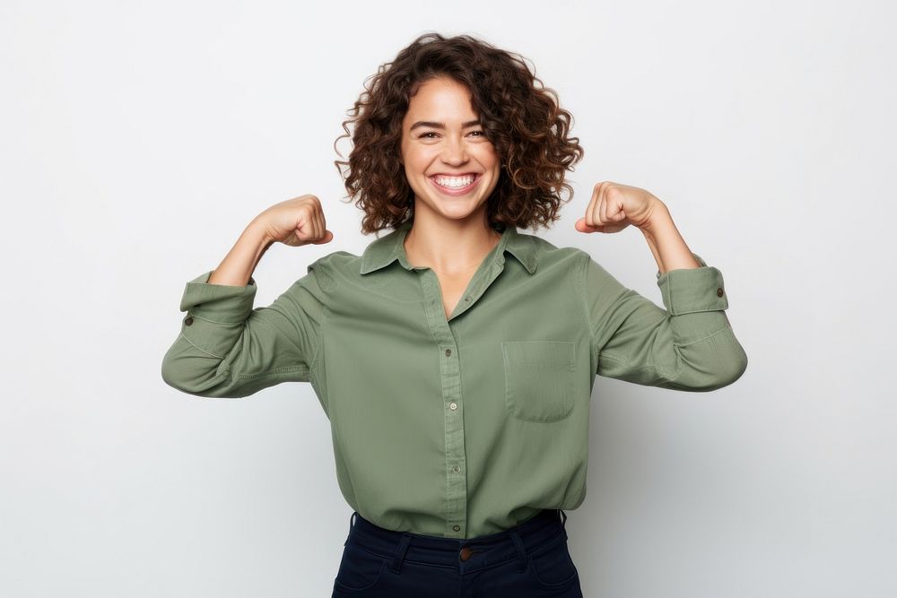 A Portrait of confident strong happy young woman looking at camera with smile and flexing her arm laughing standing…