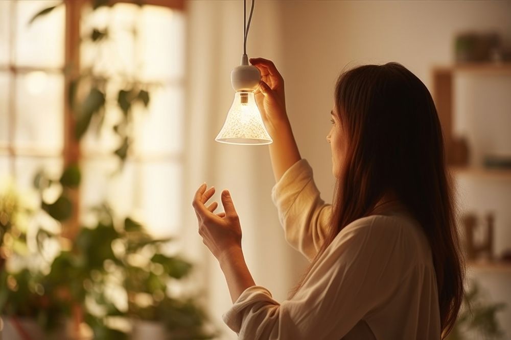 A Woman changing light bulb in hanging lamp at home adult woman architecture. AI generated Image by rawpixel.