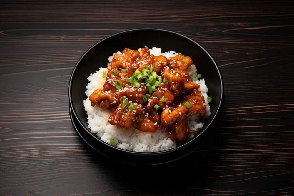 A korean fries chicken on top of the rice in the black bowl on the black wood table food meat chopsticks. AI generated Image…