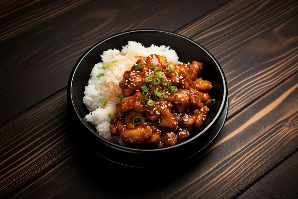 A korean fries chicken on top of the rice in the black bowl on the black wood table food meat chopsticks. AI generated Image…