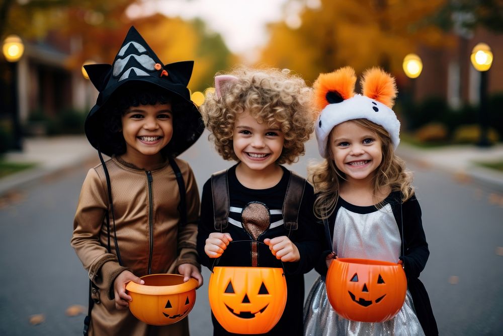 Three kids wearing full halloween costume asking for trick or treat candy from a pumpkin bowl that a woman carry child face…