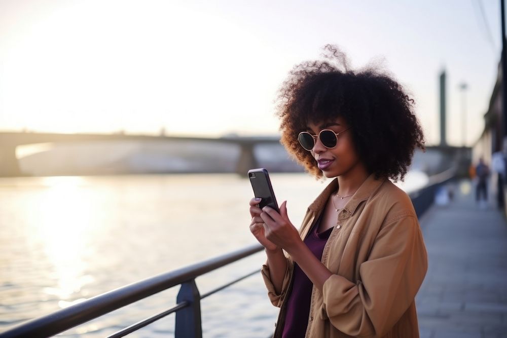Black woman with cell phone standing at the waterfront glasses travel adult. AI generated Image by rawpixel.