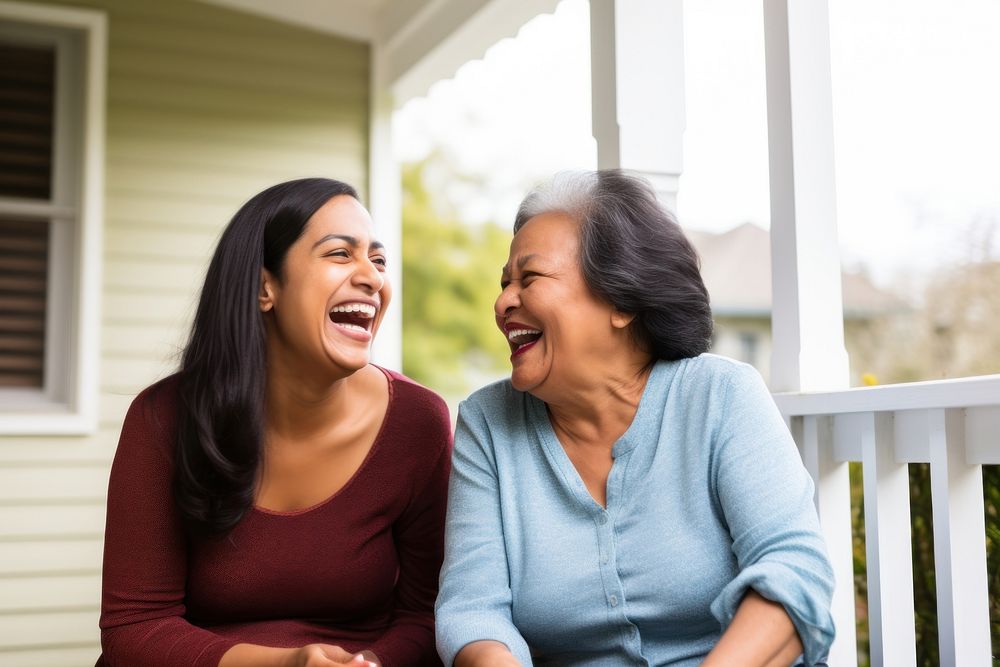 Hispanic Senior woman and adult daughter laughing on porch togetherness affectionate architecture. AI generated Image by…