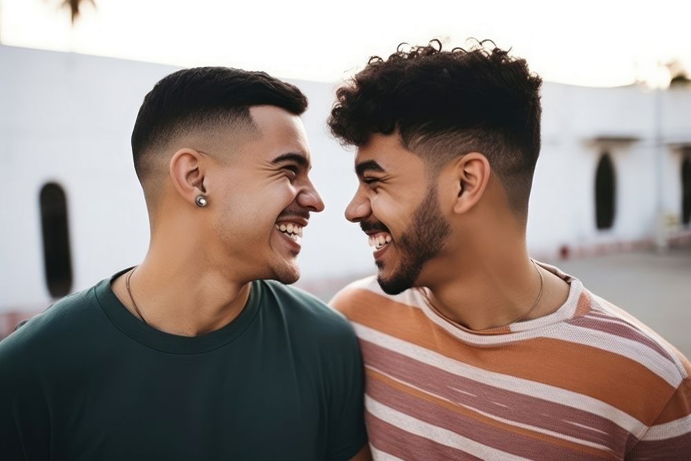 Latinx Two happy smiling friends from lgbt community standing looking at each other together laughing adult togetherness. AI…