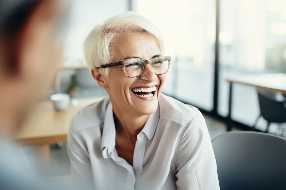 Mature businesswoman wearing eyeglasses laughing during meeting at office adult conversation togetherness. AI generated…
