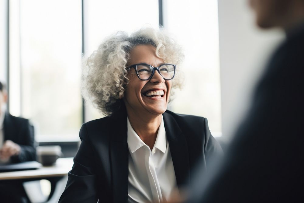 Mature businesswoman wearing eyeglasses laughing during meeting at office adult smile conversation. AI generated Image by…