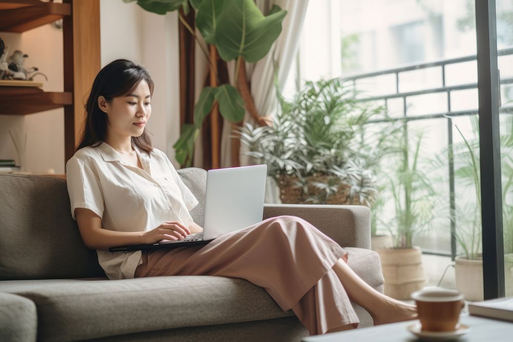 Thai woman working at home sitting furniture computer. AI generated Image by rawpixel.