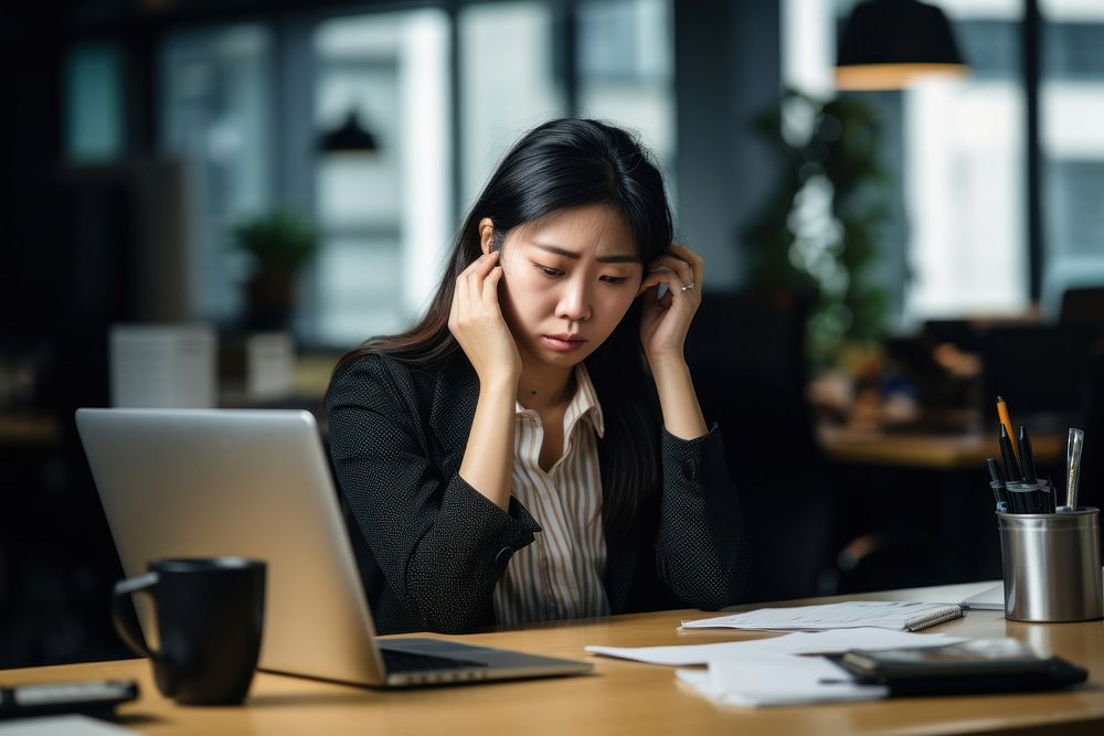 Singaporean businesswoman on the phone in the office with headache and phone computer worried laptop. AI generated Image by…