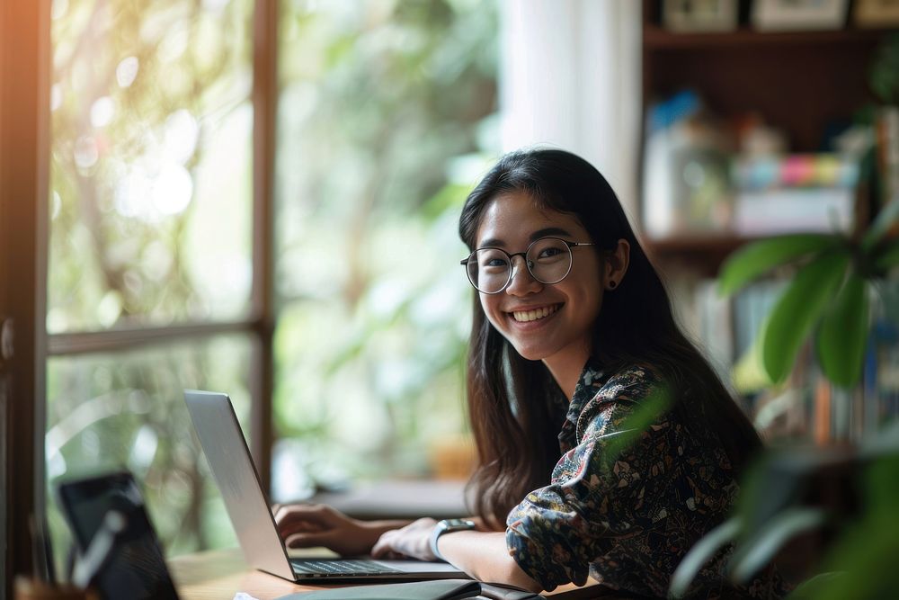 A smiling girl doing work at home laptop computer glasses. AI generated Image by rawpixel.