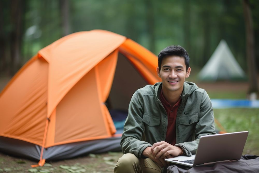 A young man with laptop in front of tent at camping recreation outdoors sitting. AI generated Image by rawpixel.