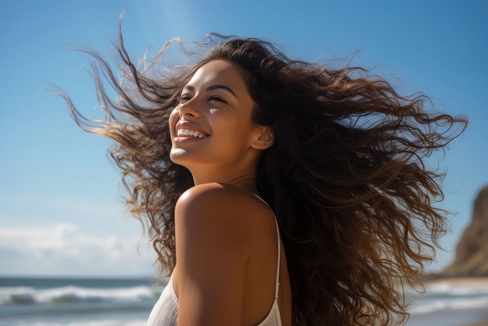 A Latina Brazilian woman standing with her hair gathered by the seaside laughing summer smile. 