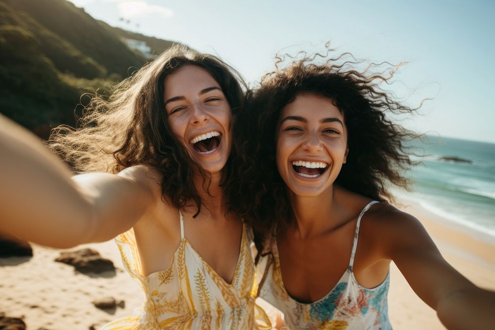 Two Latina Brazilian women friends joyfully raising their hands and dancing by the seaside laughing summer selfie. AI…