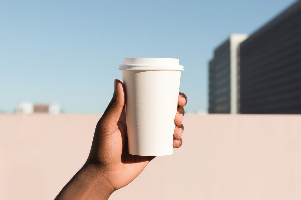Brown skin person hand holding white paper coffee cup drink mug architecture. AI generated Image by rawpixel.
