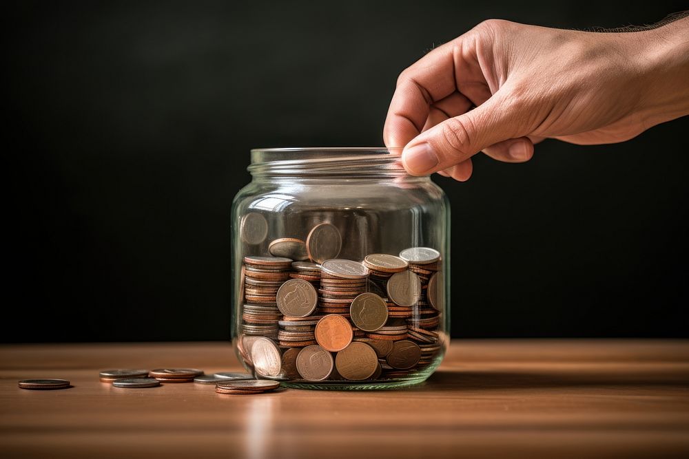 Hand holds a coin jar table investment. AI generated Image by rawpixel.